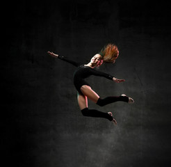 Fototapeta na wymiar girl gymnast in black sport body and uppers jumping and making dymnastic pose in air over dark background