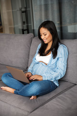 Photo of happy pregnant woman smiling and typing on laptop