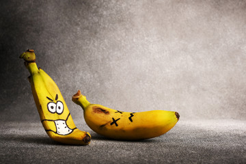 The skin of a banana with a face drawn on and a medical mask, lying next to a dead banana