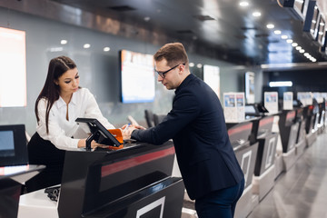 Business trip. Handsome young businessman in suit holding his passport and talking to woman at airline check in counter in the airport - 341359674