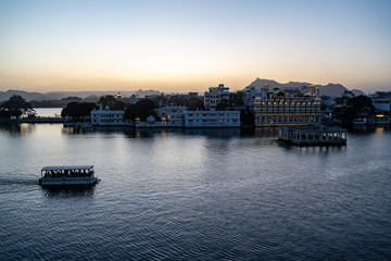 Naklejka premium Udaipur, Rajasthan India - Sunset evening view of Lake Pichola as a passenger ferry boat sails by