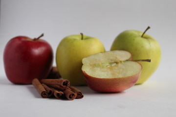 a few apples yellow green and red lie side by side on the table on a white background with cinnamon...