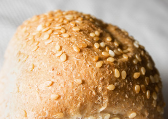 A close up of the crust of a dinner roll with sesame seeds.