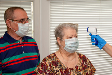 A doctor in blue latex gloves measures body temperature with an infrared emitter for a man and a...
