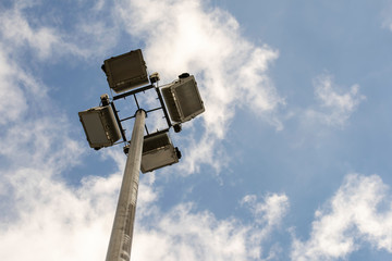 Searchlights on a pole against a blue sky with clouds.