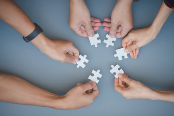 The hands of a variety of people including the Asian jigsaw puzzle And gather parts to find suitable partners to support teamwork to find common problem solving concepts, close-up perspectives