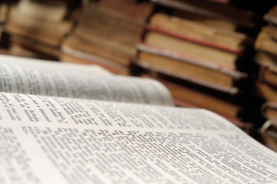 A close up image of an opened bible with various old foxed books in the background.