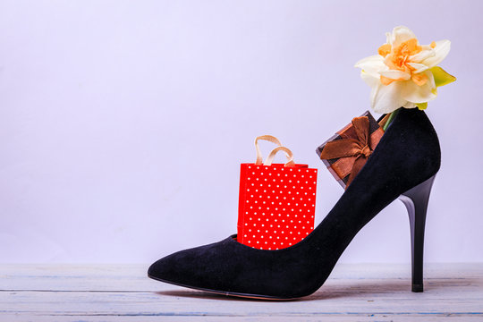 Present box in black shoe on white wooden table. Flower, gift and footwear. Many presents better than one. Mother or woman day concept.