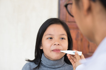 sick little girl with thermometer in mouth. unwell kid with chamber inhaler for cough treatment....