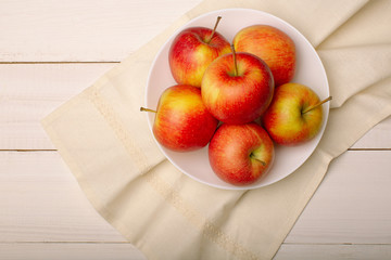 
Ripe red apples in a bowl on white wooden table, top view.
