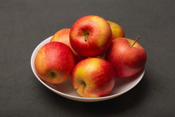 Fresh ripe red apples in white bowl on black background, close up