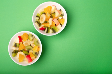 Fototapeta na wymiar Fruit salad bowls on green background top view, copy space. Diet food concept