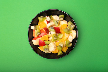 Healthy fruit salad in black bowl on the green background, top view. Summer fruit concept.