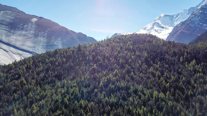 A massive mountain wall in Himalayas seen from Annapurna Circuit Trek, Nepal. Sharp and steep slopes of the mountain. There is a dense forest in front. Harsh landscape. Serenity and calmness.