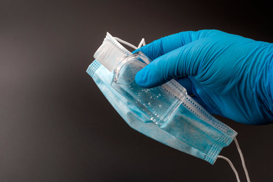 Viral sickness, coronavirus prevention and covid 19 spread concept with surgeon wearing medical gloves and holding surgical mask and alcohol based hand sanitizer gel isolated on black with copy space