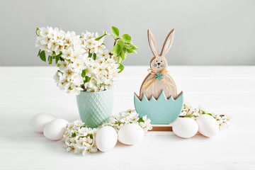 Easter bunny and White Easter eggs and spring branch with flowers on wooden background. Spring...