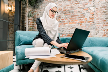 Smart attractive muslim businesswoman using laptop for working online, writing e-mail to her business partners. Arabian businesswoman in hijab working in modern office hall, using laptop