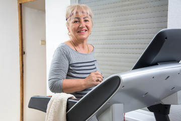 Active senior woman running on treadmill machine at home.