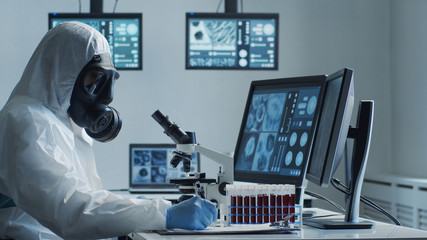 Scientist in protection suit and masks working in research lab using laboratory equipment:...
