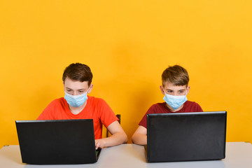 Boys in medical masks are on distance learning and are sitting in front of a laptop monitor, due to the threat of a coronavirus pandemic.