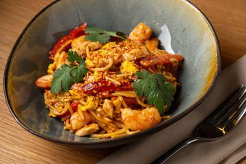 WOK udon noodle with chicken and vegetables in white plate on wooden background