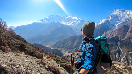 Man taking a selfie while trekking on the Annapurna Circuit Trek, Himalayas, Nepal. Snow caped Annapurna chain in the back. Lots of dried grass. High altitude, massive mountains. Freedom and adventure