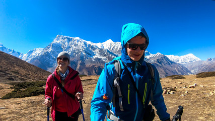 A couple trekking along Annapurna Circuit Trek in Himalayas, Nepal. Snow caped Annapurna chain in the back. Barren, dried and harsh landscape. The couple enjoys their hike. Adventure and exploration.