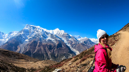 A woman trekking on the Annapurna Circuit Trek, Himalayas, Nepal. Panoramic view on snow caped Annapurna chain. Lots of dried grass. High altitude, massive mountains. Freedom and adventure