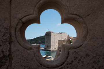 Views, through a cross-shaped hole located in a bridge, of the stone walls and the port in Dubrovnik, Croatia, Europe.