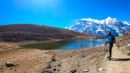 A man trekking along the Ice Lake, Annapurna Circuit Trek detour, Himalayas, Nepal, surrounded by high, snow caped mountains. Annapurna Chain in the back. High altitude lake. Harsh landscape.