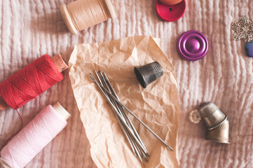 Thread spools with needles, buttons and thimbles on textile closeup. Top view. Handmade. Work at home.