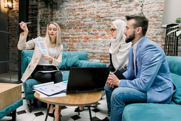 Group of three focused multiethnic male and female business people in formal clothes gathered...