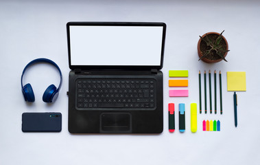 Modern white office desk table with laptop, smartphone, headphones and other supplies. Top view, flat lay.