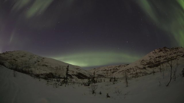 Beautiful aurora borealis in night sky over snowy mountains and field time laps. Green and yellow colors night lighting in northern winter landscape. Natural northern phenomenon timelapse.