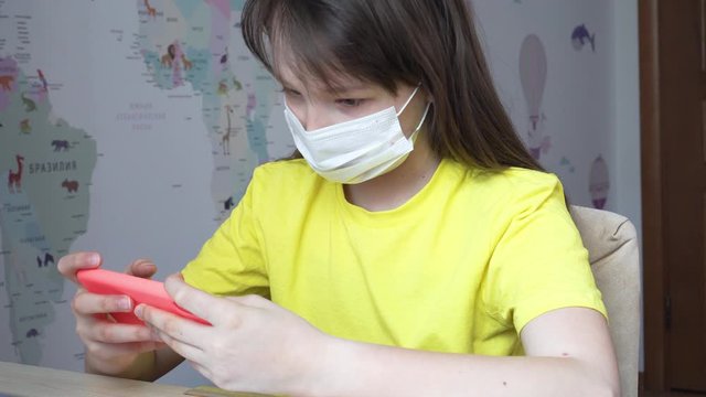 a child in a medical mask plays a game on the phone. concept of children&rsquo;s passion for games in a smartphone. 