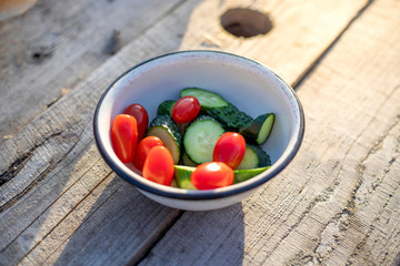 Fresh cucumbers and tomatoes in a white plate on a wooden table, top view.