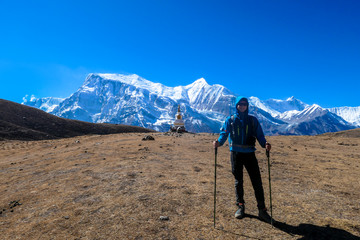 A man trekking on the Annapurna Circuit Trek, Himalayas, Nepal. Panoramic view on snow caped Annapurna chain. Lots of dried grass. High altitude, massive mountains. Freedom and adventure