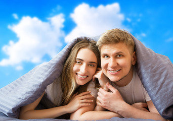 Obraz premium Happy beautiful couple in bed isolated on blue sky background, stay at home concept, coronavirus quarantine background, self isolation, life style at home
