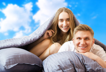 Happy beautiful couple in bed isolated on blue sky background, stay at home concept, coronavirus quarantine background, self isolation, life style at home