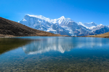 Fototapeta na wymiar A close up on the Ice lake, along the Annapurna Circuit Trek in Himalayas, Nepal. Annapurna chain in the back, covered with snow. Clear weather, dry grass. Freedom, solitude, chill and relaxation