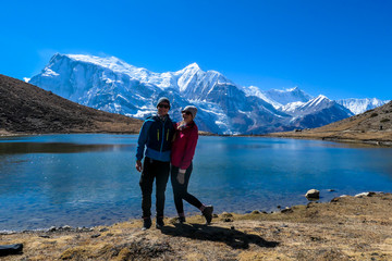 A couple in hiking outfits standing at the shore of Ice Lake, Annapurna Circuit Trek, Himalayas, Nepal. They are having fun. High, snow caped Annapurna chain in the back. Happiness and love