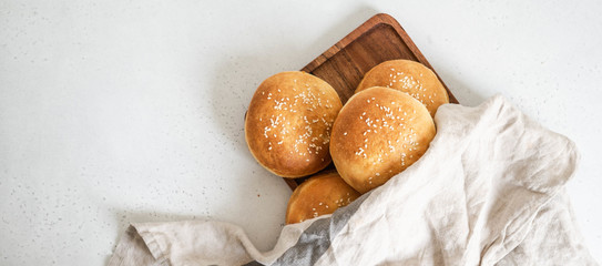 Group crisp fresh homemade buns with sesame on wood tray under a linen towel on a table. Food...