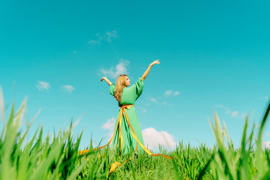 Young woman wearing a green dress standing in a field with ribbons wrapped around her waist