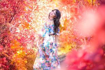 Outdoor atmospheric photo of young beautiful woman in long dress in red autumn wood. Brown hair and eyes. Warm and sunny October weather