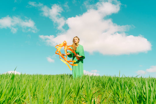 Young woman wearing a green dress standing in a field with blowing ribbons