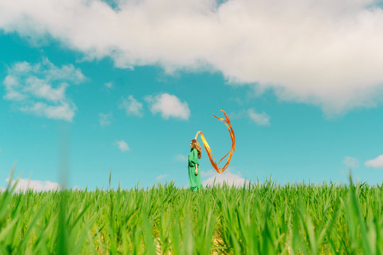 Young woman wearing a green dress standing in a field with blowing ribbons
