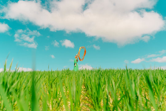 Young woman wearing a green dress standing in a field with blowing ribbons