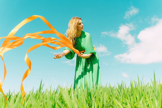 Young woman wearing a green dress standing in a field with blowing ribbons