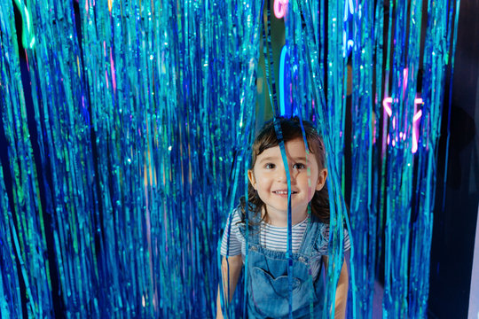 Portrait of smiling little girl among blue metallic curtain in a party room