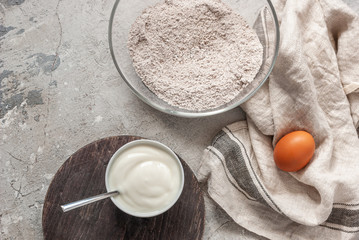 Ingredients for bird cherry cake. Flour mixture with bird cherry, egg and yogurt on a gray concrete table next to a beige towel. copyspace cooking recipe